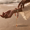 Person wearing the Balance + Clarity Meditation Bracelet, a beaded bracelet on a beach with sunset in the background