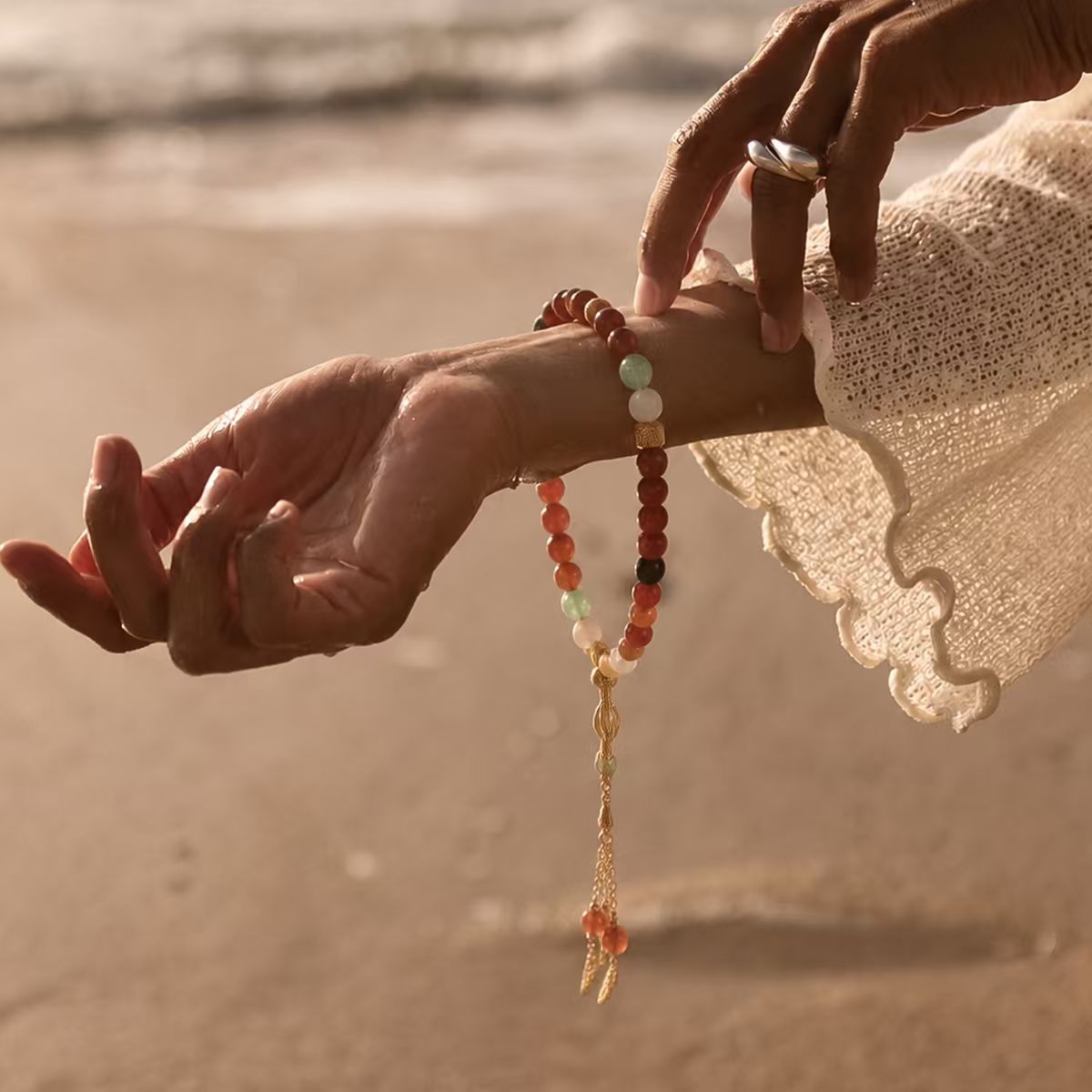 Person wearing the Balance + Clarity Meditation Bracelet, a beaded bracelet on a beach with sunset in the background