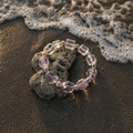 Chrysaora Colorata bracelet with purple and clear beads on a beach with waves.