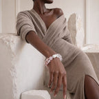 Woman wearing a beige sweater and bracelet with pink stones in a soft, neutral-toned room.