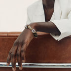 The Gold | Edge Bracelet shown on a model's wrist resting on a brown leather chair, emphasizing the contrast between the black onyx beads and the white blazer.