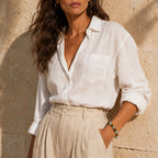 Woman wearing a white linen shirt and beige pants against a stone wall.