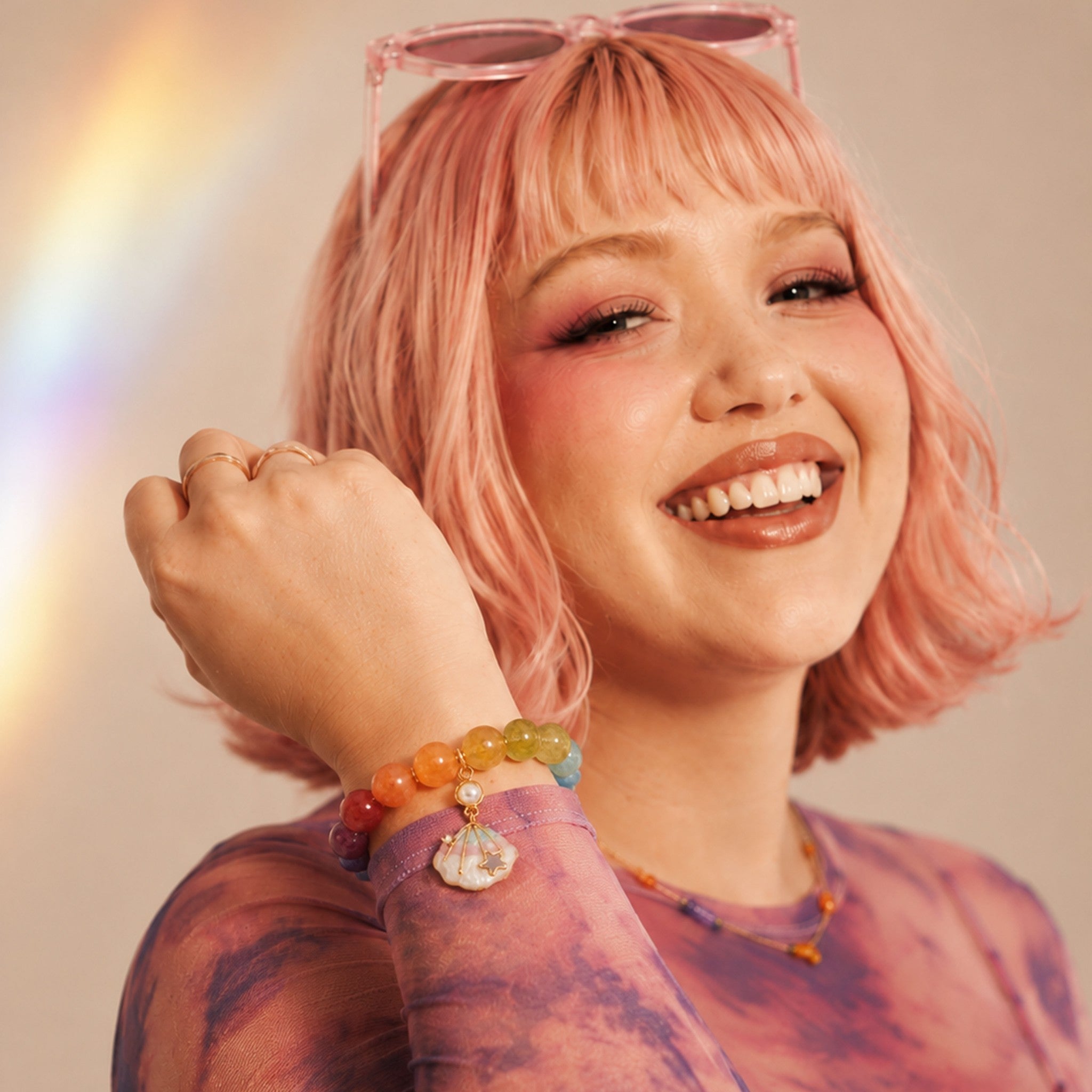Woman with pink hair and colorful bracelets smiling against a neutral background