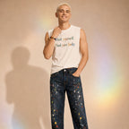 Person wearing a sleeveless shirt with text and colorful jeans against a beige background