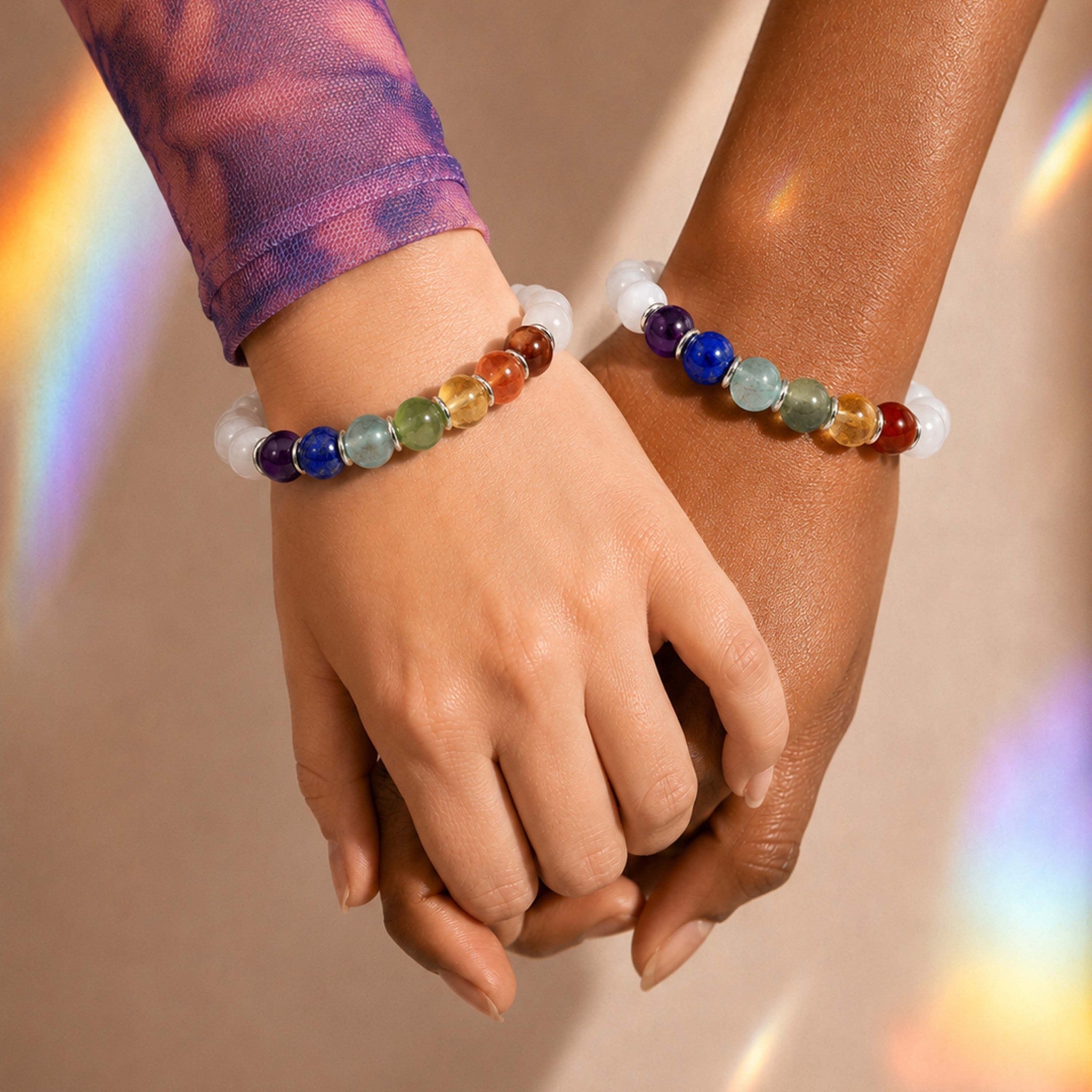 Two hands holding each other wearing colorful beaded bracelets on a neutral background