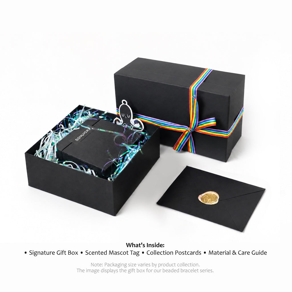 Black gift box with rainbow ribbon, scented mascot tag, and collection postcards on a white background.