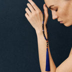 Woman wearing the Reason + Clarity Meditation Bracelet, a beaded bracelet with a blue tassel against a dark background