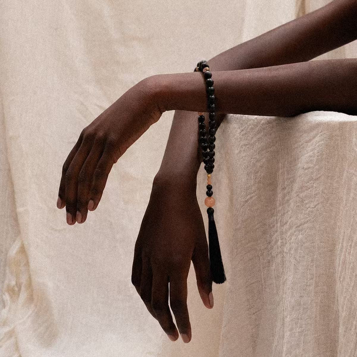 Person wearing the Release + Recovery Meditation Bracelet, a black beaded bracelet with tassel on a beige background