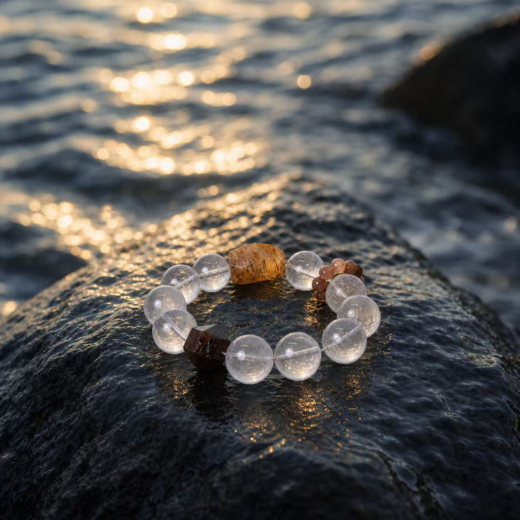 Handcrafted Turritopsis Nutricula Crystal Bracelet inspired by marine life, showcasing transparent round crystals and earthy accents on a coastal rock against sunlit ocean waves.